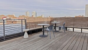 Terraço no telhado com piso de madeira, guarda-corpos de metal e área de estar ao ar livre, incluindo mesas e cadeiras.