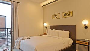 Uma cama bem arrumada em quarto de hotel com vista exterior, mesa de cabeceira com abajur e placas de sinalização na parede.
