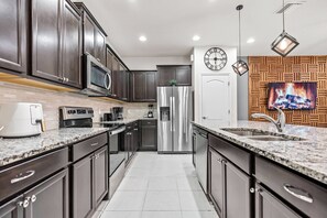 A modern kitchen with dark cabinets, stainless steel appliances, granite countertops, and a built-in oven. - 5BR townhouse sleeps 13 with private pool (Kissimmee)