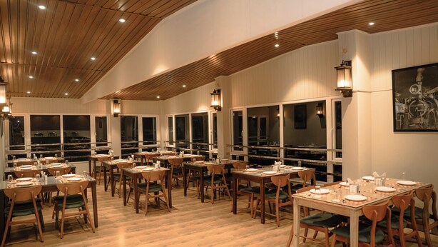A restaurant with multiple tables and chairs, wooden ceiling, and large windows. - arjay valley (Darjeeling)