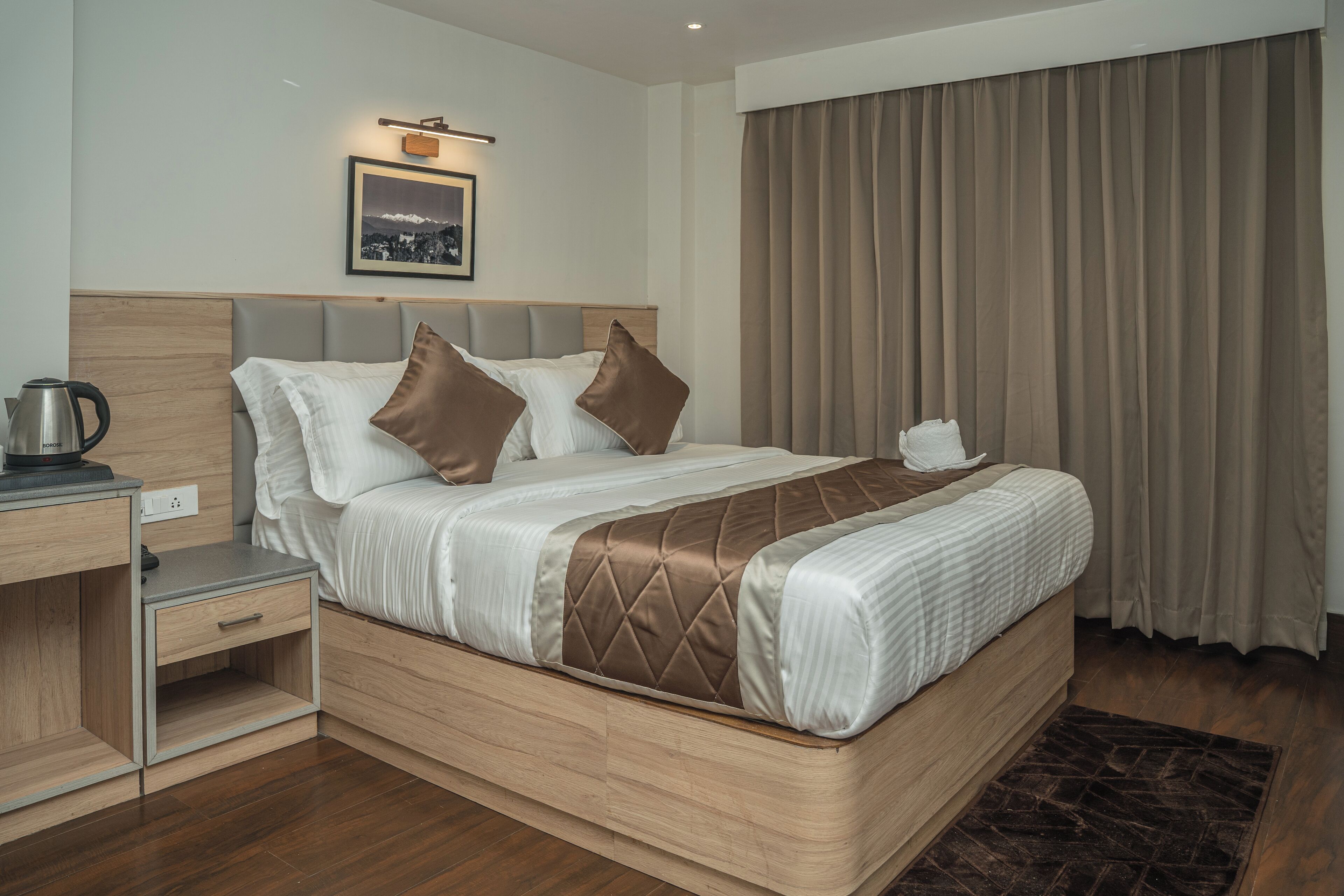 Een moderne hotelkamer met een houten bed, een nachtkastje, een waterkoker en een ingelijste foto aan de muur.