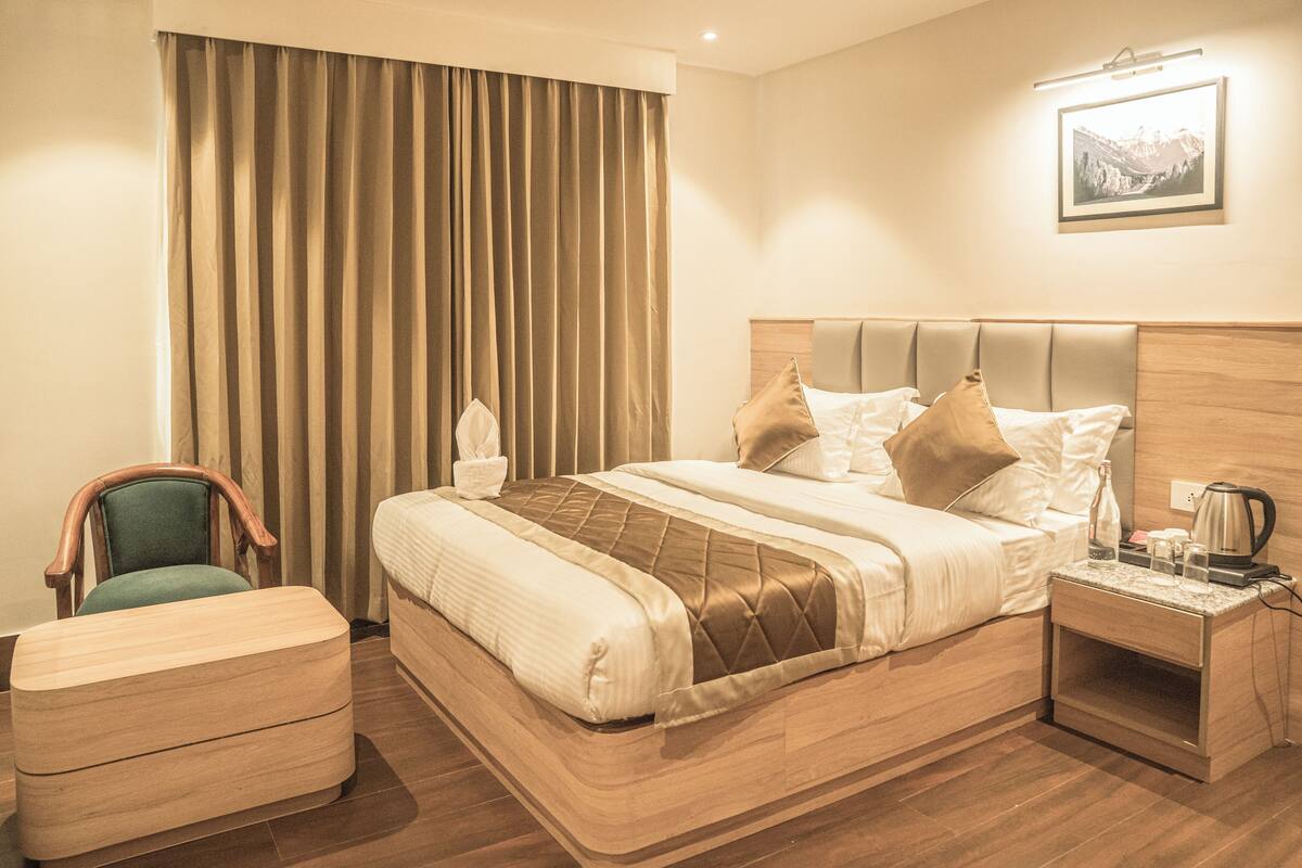 A hotel room with a large bed, a wooden nightstand, a chair, and a view of the mountains through the window.