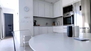 A modern kitchen with white cabinets, a round dining table, and a coffee machine. - Panorama Beach - Penthouse (Torrox)