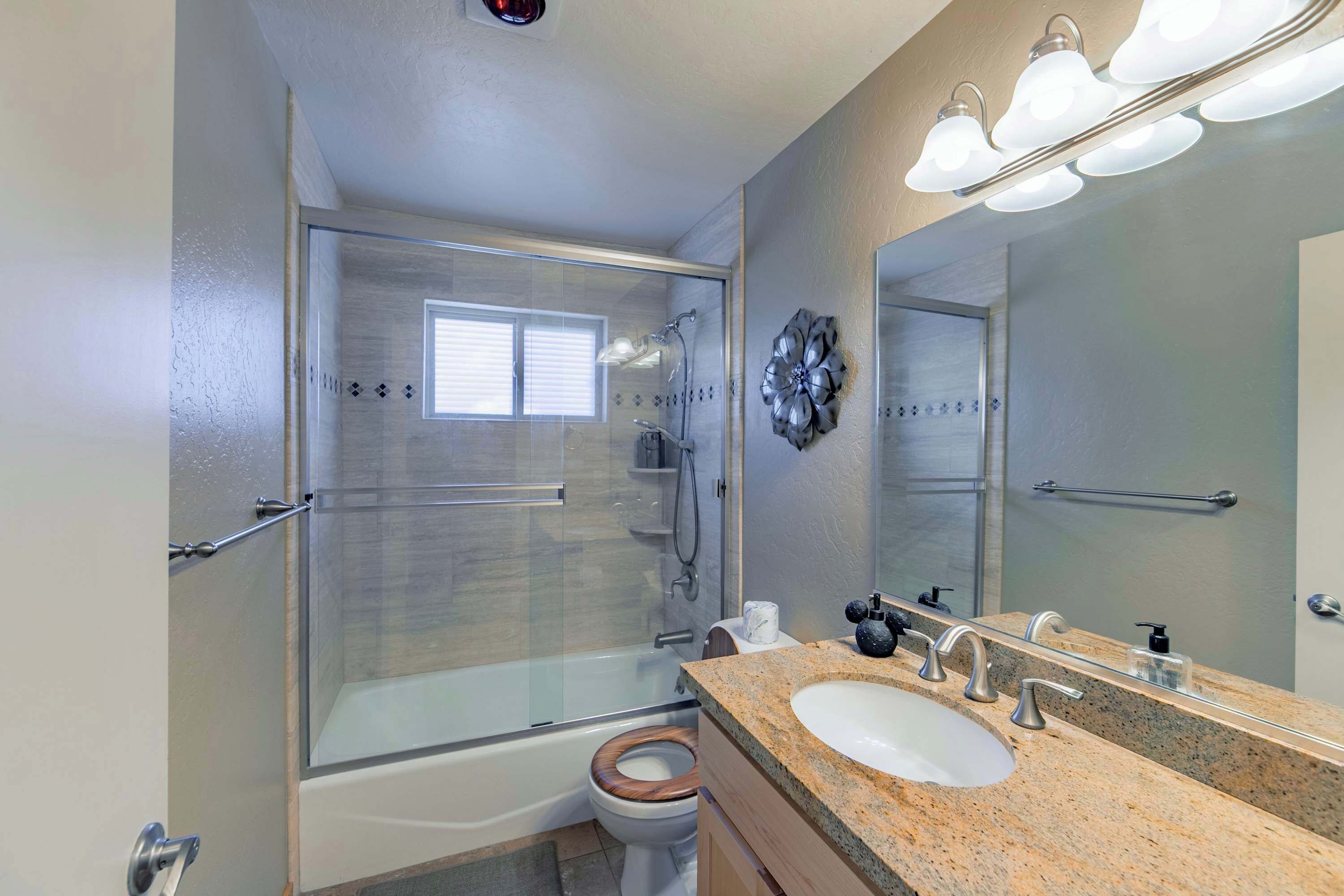A modern bathroom with a glass-enclosed shower, a white toilet, a granite countertop, and a large mirror.