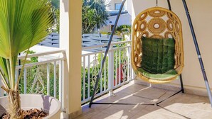 A balcony with a hanging chair, a potted plant, and a view of a blue-roofed building. - Casa Verde: Grand Case Village (Grand-Case)