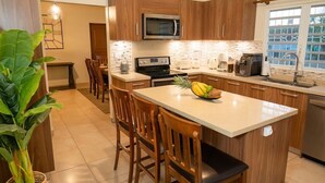 A modern kitchen with wooden cabinets, a central island with chairs, a microwave, a stove, and a sink. - Casa Verde: Grand Case Village (Grand-Case)