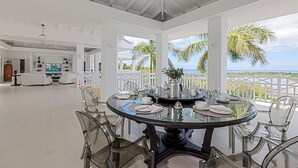 Un comedor amplio con una mesa y sillas de vidrio, una cocina al fondo y vista al océano.