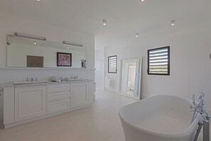 Ein geräumiges Badezimmer mit einer großen Badewanne, einem doppelten Waschbecken mit zwei Becken und einem großen Spiegel darüber.