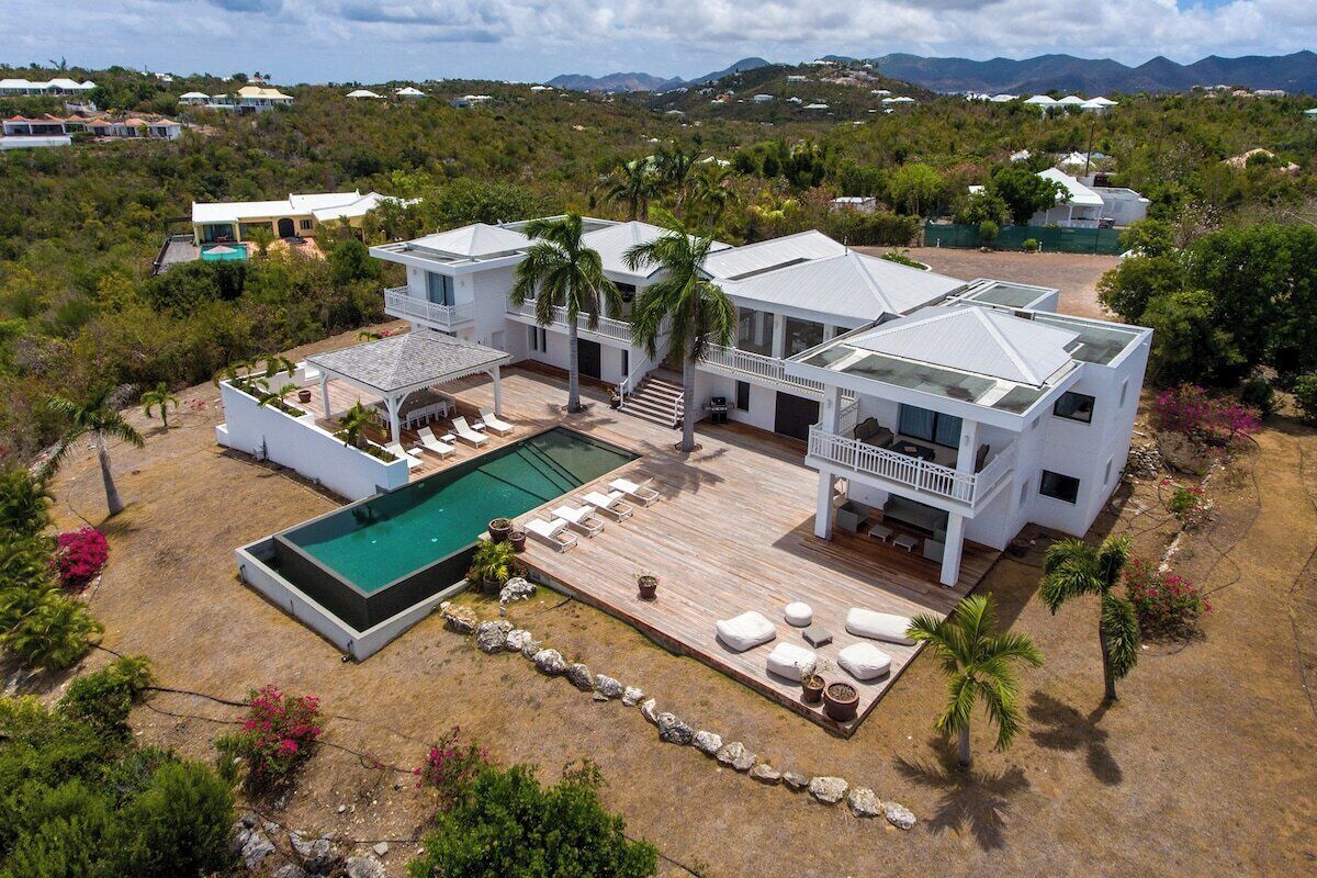 A large, modern house with a pool, multiple decks, and a view of the surrounding landscape.