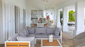 Una sala de estar moderna con un sofá seccional gris, una mesa de centro de madera y un comedor con una mesa y sillas blancas.