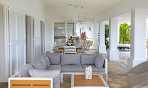 Ein modernes Wohnzimmer mit einem grauen Ecksofa, einem Holztisch und einem Essbereich mit weißem Tisch und Stühlen.