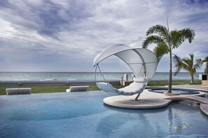 Un espace piscine agrémenté d’un fauteuil suspendu, de palmiers et offrant une vue sur l’océan.