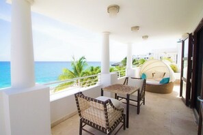 Ein Balkon mit Blick auf das Meer, Korbmöbel und eine überdachte Sitzecke.