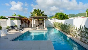 A swimming pool with lounge chairs and a pergola, surrounded by greenery and white walls. - Beach Front Condo   AMAZING PLACE TO SPEND YOUR VACATION Unit #301 (Simpson Bay)