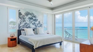 A bedroom with a large bed, a ceiling fan, and a view of the ocean through large sliding doors. - Beach Front Condo   AMAZING PLACE TO SPEND YOUR VACATION Unit #301 (Simpson Bay)
