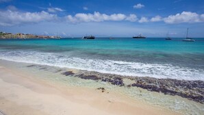 A beach with clear turquoise water, a sandy shore, and several boats in the distance. - Beach Front Condo   AMAZING PLACE TO SPEND YOUR VACATION Unit #301 (Simpson Bay)