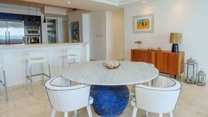 A modern kitchen with stainless steel appliances, a white dining area with a round table and white chairs, and a wooden cabinet with decorative items. - Beach Front Condo   AMAZING PLACE TO SPEND YOUR VACATION Unit #301 (Simpson Bay)