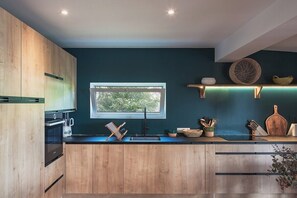 A modern kitchen with wooden cabinets, a black countertop, a window, and various kitchen utensils. - Baltazar   Idyllic Sunrises & Stunning ocean views (Cul-de-Sac)
