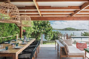 An outdoor dining area with wooden tables and chairs, a wicker hanging light fixture, and a view of the sea. - Baltazar   Idyllic Sunrises & Stunning ocean views (Cul-de-Sac)