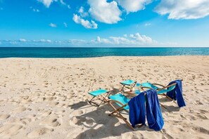 Ein Strand mit vier blauen Liegestühlen und einem Tisch mit einem Getränk.