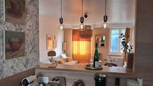 A modern kitchen with a toaster, kettle, and coffee maker on the counter, a bottle of wine on the table, and a mirror reflecting the living room. - Large, cozy, quiet family apartment in the center of town, with view of the cathedral (Strasbourg)