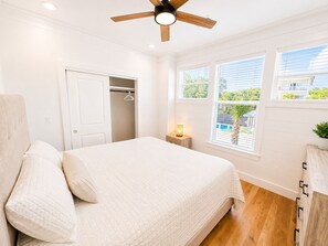 Ein Schlafzimmer mit einem Bett, einem Deckenventilator, einem Nachttisch mit Lampe, einem Kleiderschrank und einem Fenster mit Jalousien.