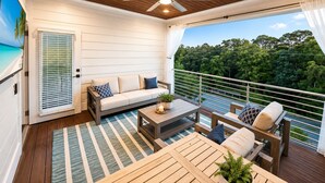 A balcony with a wooden ceiling, a sofa, a table, and a view of a lush green landscape. - Luxury 3-Level Townhome Santa Rosa Beach Florida 30A, Walk2Beach, Golf Cart,Pool (Santa Rosa Beach)