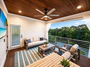 Ein Balkon mit Holzboden, einer Couch, einem Tisch und Blick auf eine üppige grüne Landschaft.