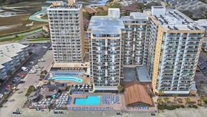 Ein Hochhaus-Hotel mit mehreren Balkonen, einem Schwimmbad und einer Strandanlage.
