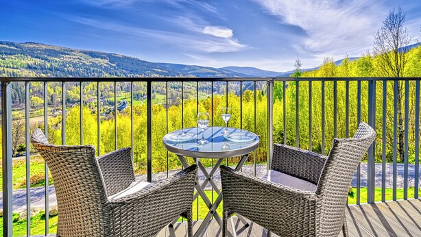 Un balcon agrémenté de meubles en osier et d’une table en verre, offrant une vue sur un paysage pittoresque.