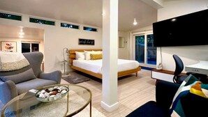 Een moderne hotelkamer met een bed, een sofa, een televisie en een zithoek met een glazen tafel.