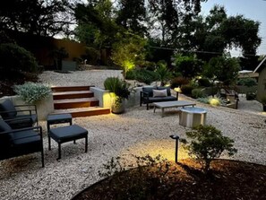 Un espace extérieur aménagé en patio, avec des coins salon, un petit escalier et un jardin.