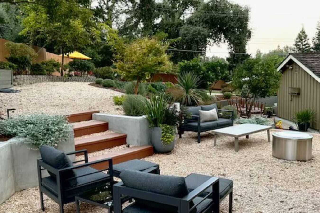 A patio area with outdoor furniture, steps leading to a deck, and various potted plants.