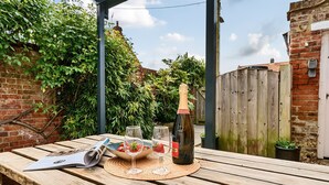 Een houten tafel met een krant, twee wijnglazen, een fles wijn en een schaal aardbeien.