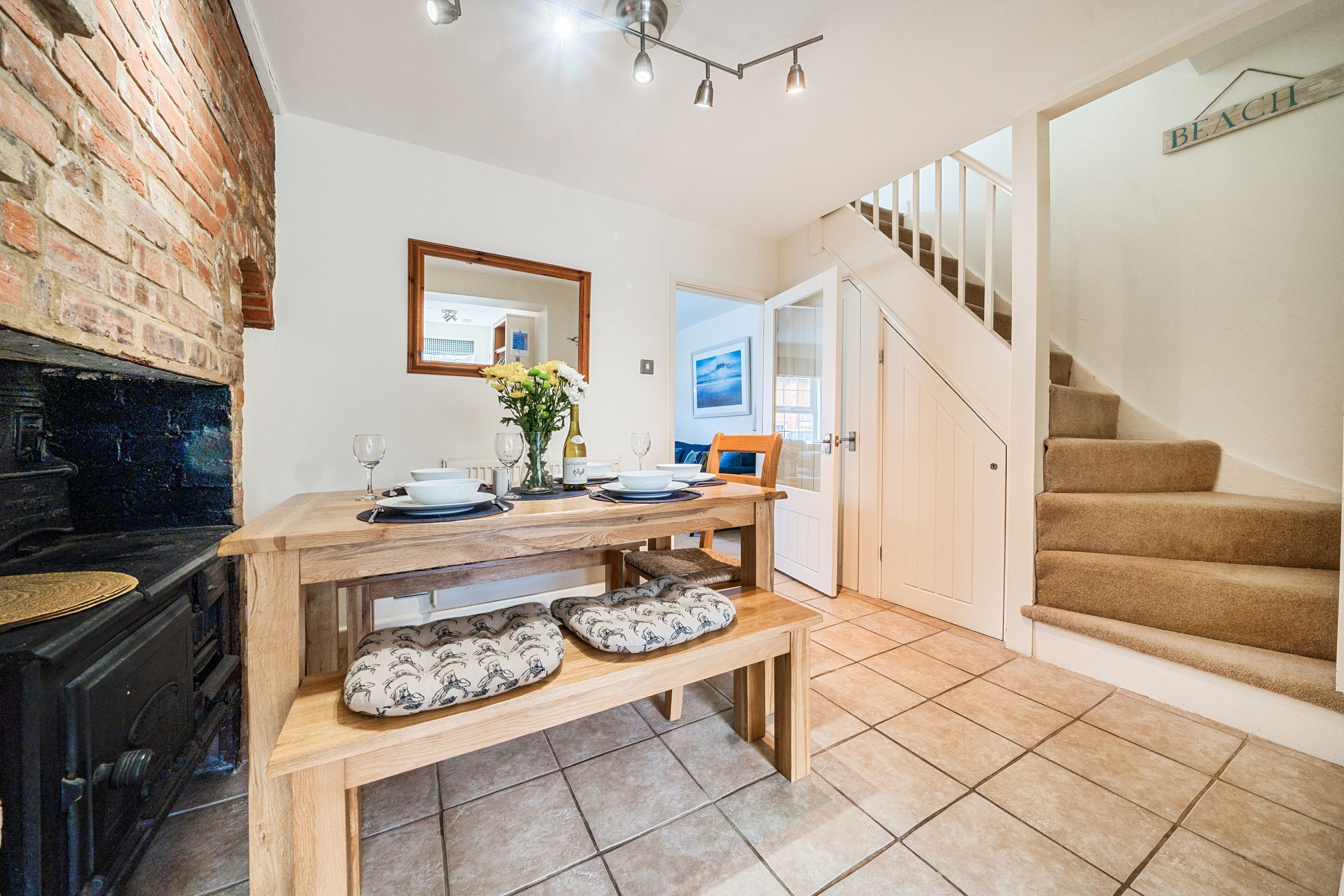 A kitchen with a brick wall, wooden table, bench, and a staircase leading to a bedroom.