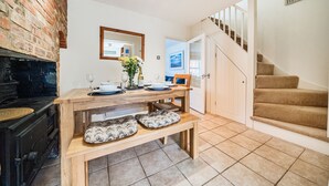 Een keuken met een bakstenen muur, een houten tafel, een bankje en een trap die naar een slaapkamer leidt.