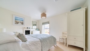 Een slaapkamer met een bed, een dressoir, een stoel en een schilderij aan de muur.