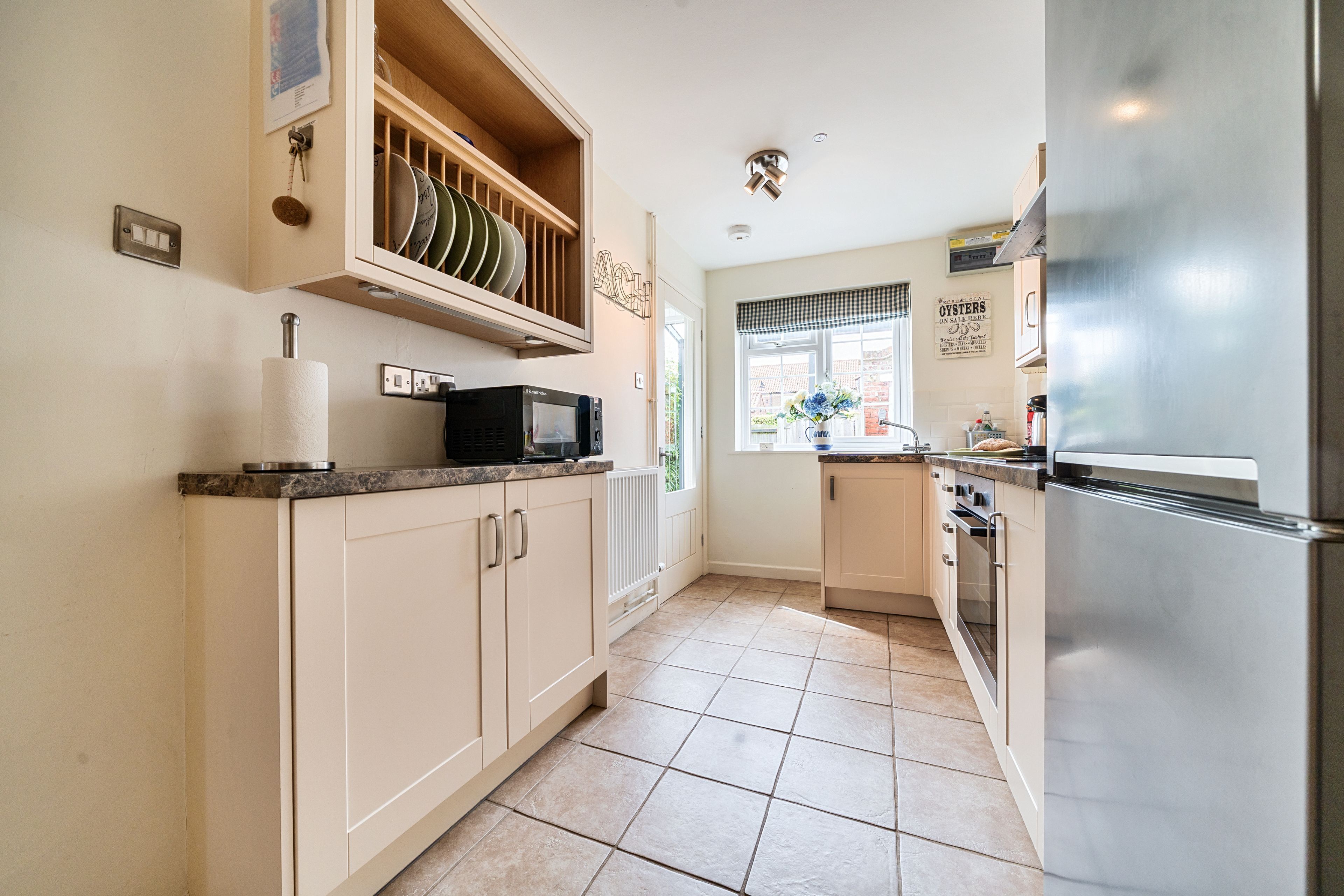 A modern kitchen with beige cabinets, a stainless steel refrigerator, a microwave, and a window with a view of the outside.