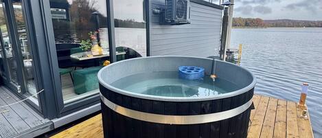 Un jacuzzi en una terraza de madera con cerramiento de vidrio y vista a un lago.