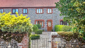 A stone building with a red-tiled roof, a wooden door, and a small garden with a metal gate. - 4 Hare Cottage - sleeps 4 guests  in 3 bedrooms (South Creake)