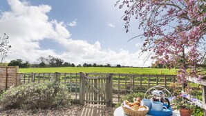 A garden table with bread, cups, and a teapot, surrounded by a wooden fence and a field. - 4 Hare Cottage - sleeps 4 guests  in 3 bedrooms (South Creake)