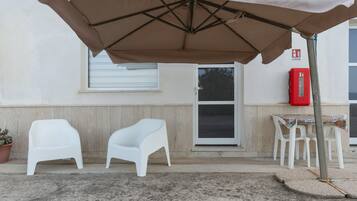 An outdoor seating area with a table and chairs, a covered umbrella, and a fire extinguisher on the wall.