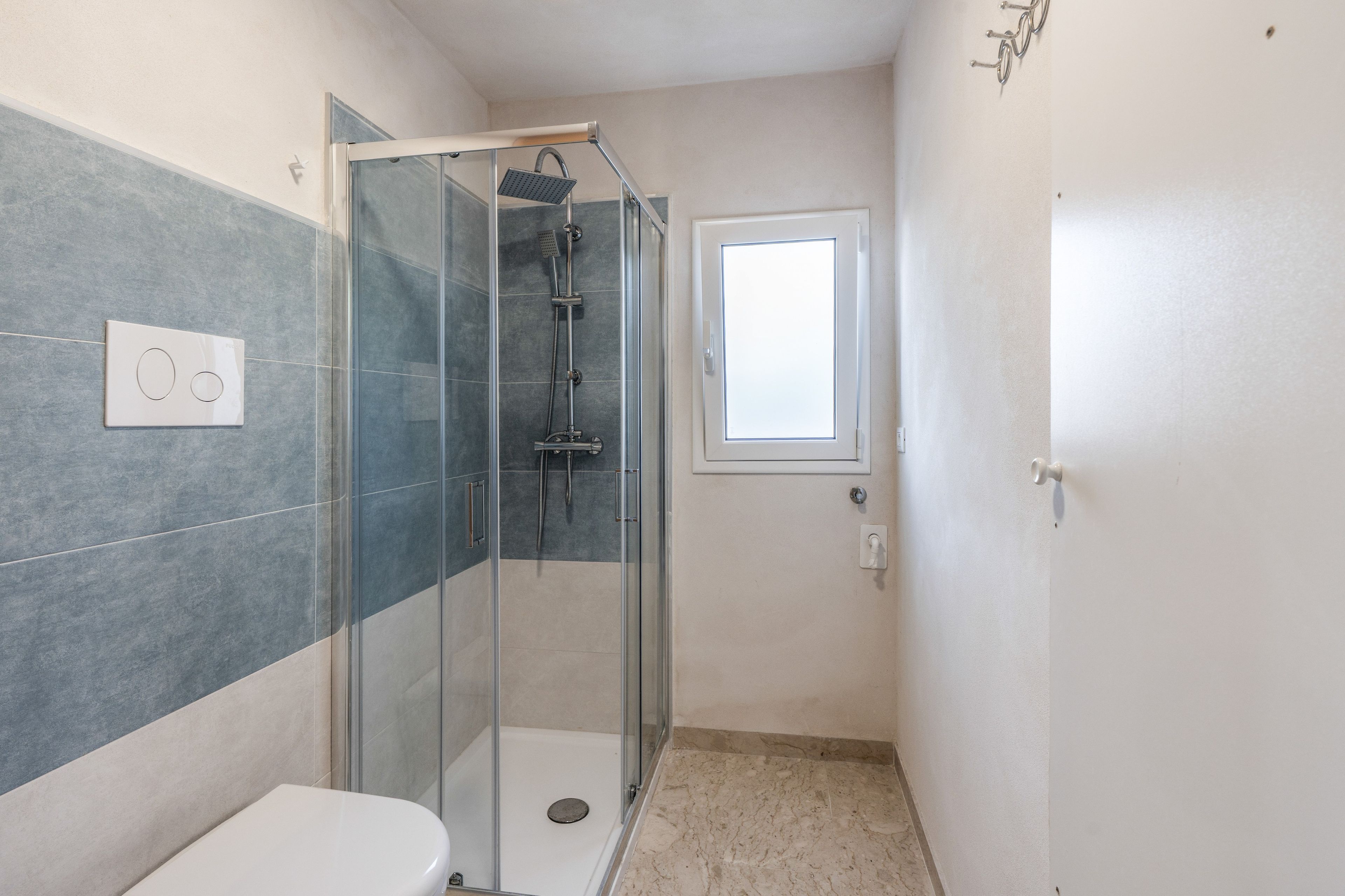 Une salle de bain avec une douche à parois de verre, des toilettes et une fenêtre.