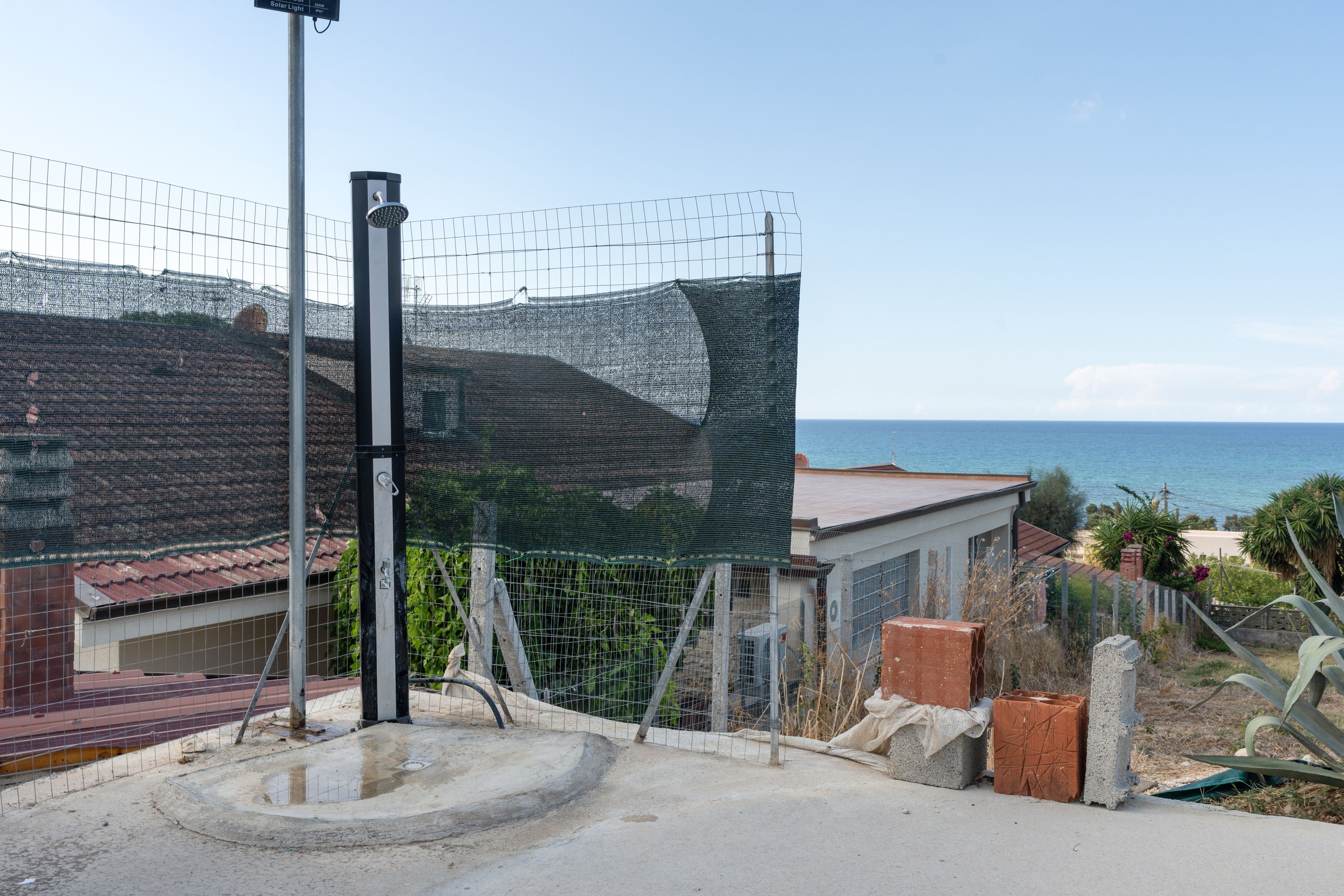 A fenced area with a concrete structure, a metal pole, and a view of the sea.