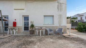 A building with a white exterior, a door, a window, and a small balcony area with a table and chairs.