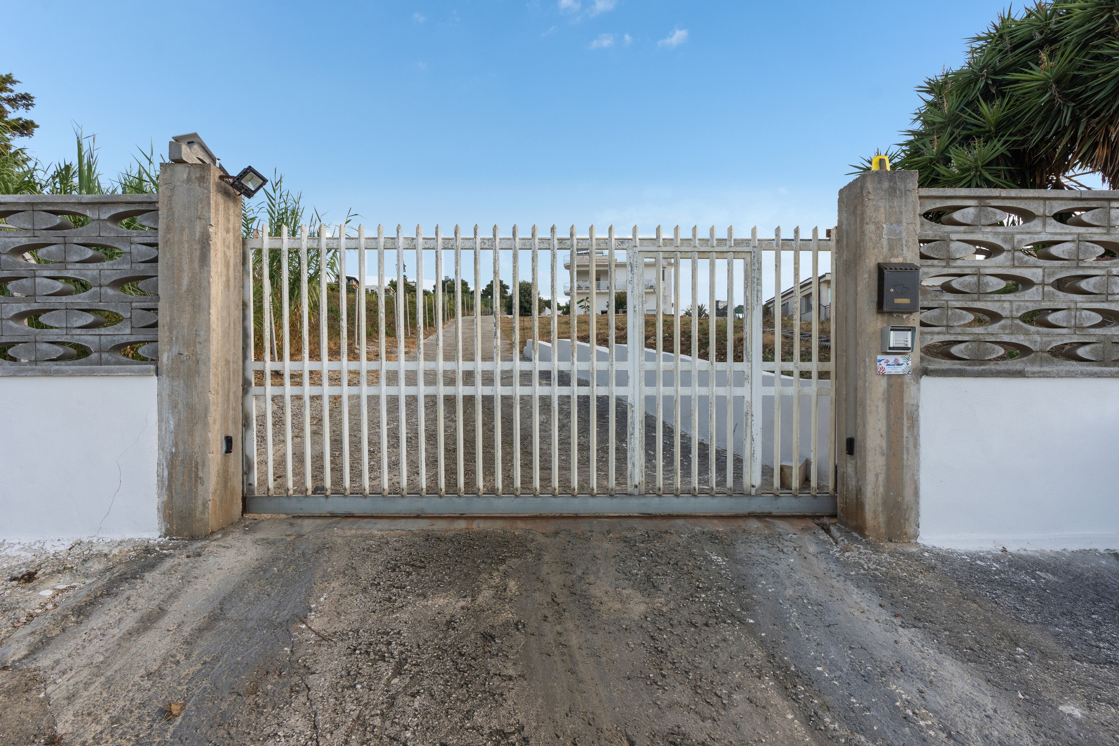 A gated entrance with a metal gate and a concrete wall with decorative cutouts.
