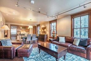 Ein geräumiges Wohnzimmer mit Ledersofa, Hocker und Couchtisch. Im Hintergrund ist ein Essbereich mit Stühlen und einem Tisch zu sehen.