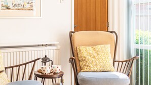 A wooden rocking chair with a patterned cushion, a small table with a polka-dotted cup and a teapot, and a framed picture on the wall.