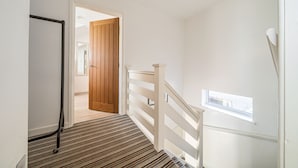 A hallway with a striped carpet, a wooden door, and a white railing with a window.