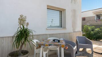 Ein kleiner Sitzbereich im Freien mit Tisch und Stühlen, einem Blumentopf und einem Fenster.
